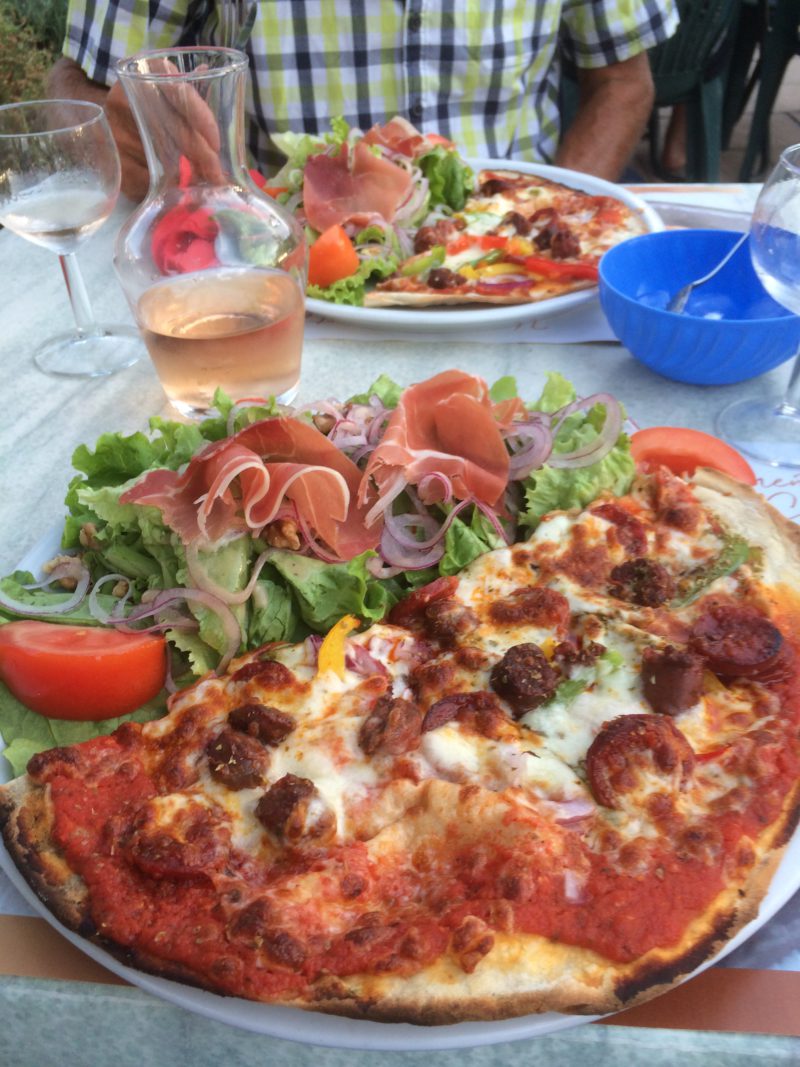 Foto van een bord met een rijke pizza en frisse salade op Camping Lei Suves